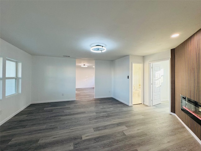 unfurnished living room with recessed lighting, a glass covered fireplace, baseboards, and dark wood-style flooring