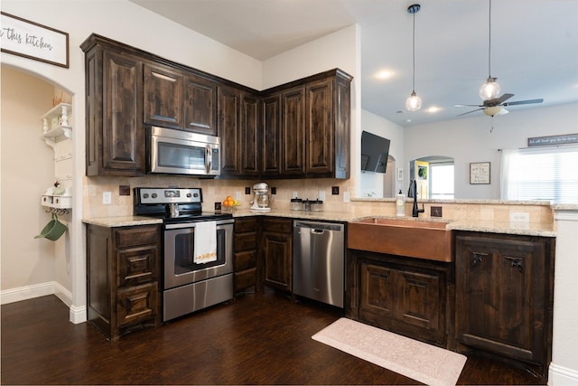 kitchen with a ceiling fan, a sink, arched walkways, dark brown cabinetry, and appliances with stainless steel finishes