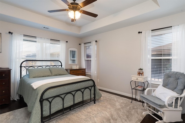 bedroom with a tray ceiling, visible vents, a ceiling fan, and baseboards