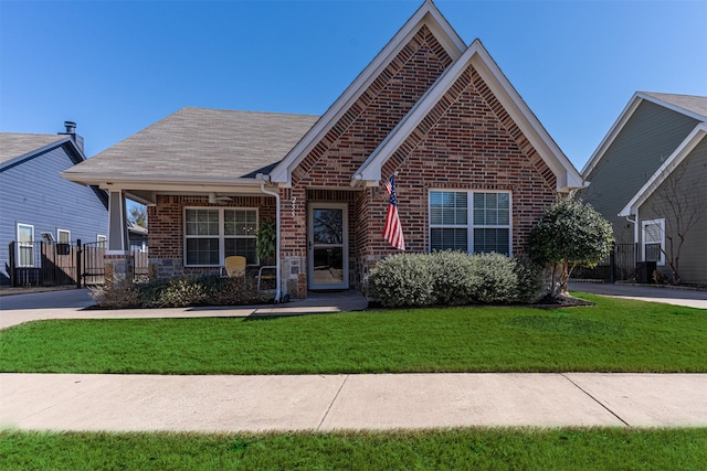 view of front facade featuring a gate, brick siding, fence, roof with shingles, and a front yard