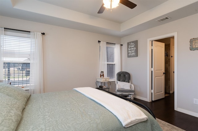 bedroom featuring baseboards, wood finished floors, visible vents, and a raised ceiling