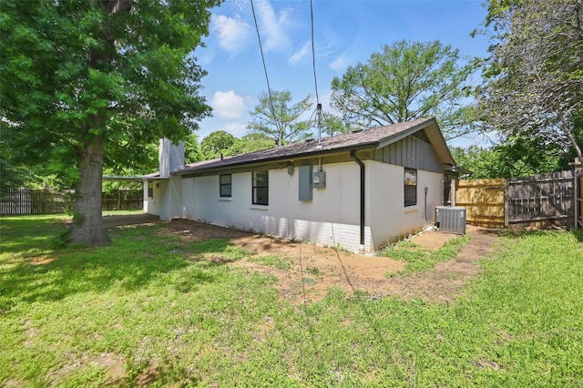 back of house featuring cooling unit, a yard, brick siding, and fence