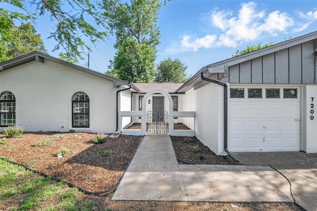 view of front of property featuring a gate, an attached garage, board and batten siding, and brick siding