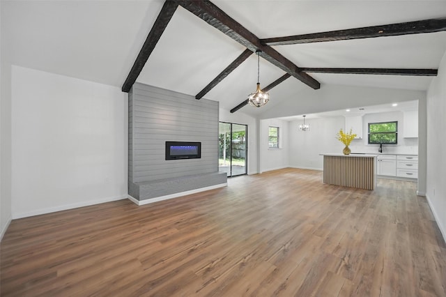 unfurnished living room with lofted ceiling with beams, an inviting chandelier, light wood-style floors, and baseboards