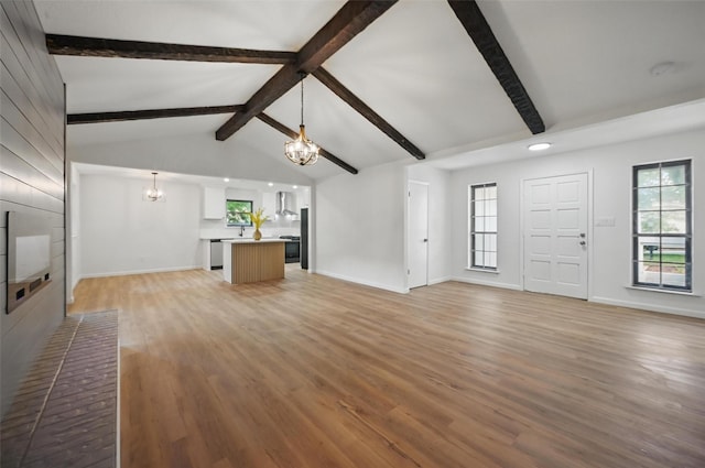 unfurnished living room featuring a chandelier, light wood-type flooring, a wealth of natural light, and lofted ceiling with beams