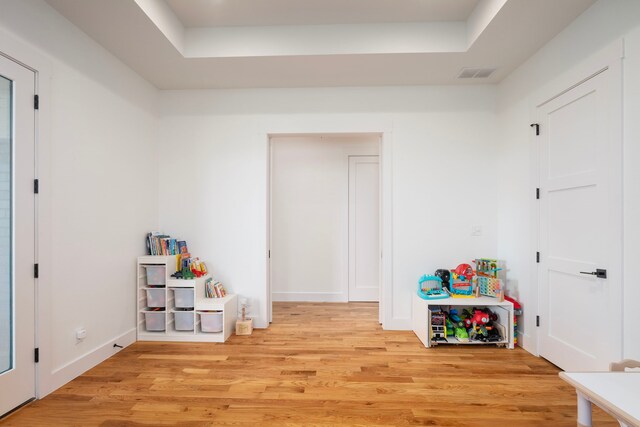rec room with baseboards, light wood-style floors, visible vents, and a raised ceiling