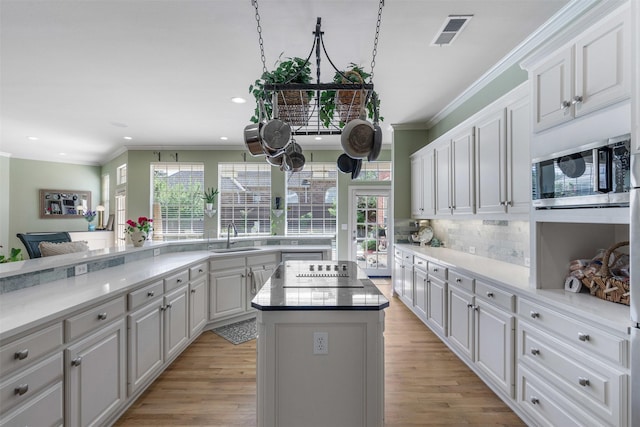 kitchen featuring a kitchen island, visible vents, black electric cooktop, a sink, and stainless steel microwave