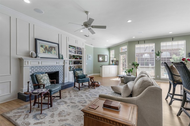 living room with crown molding, a ceiling fan, light wood finished floors, and a tile fireplace