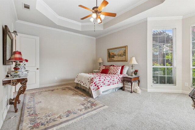 carpeted bedroom with crown molding, a ceiling fan, baseboards, a tray ceiling, and visible vents