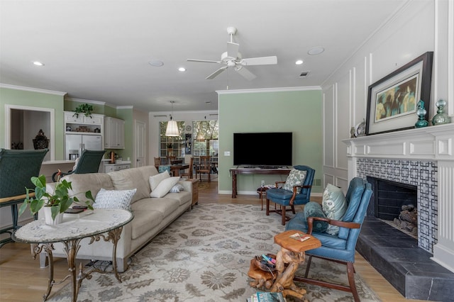 living area featuring crown molding, a fireplace, a ceiling fan, and visible vents