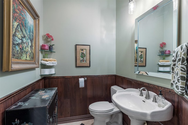 half bathroom featuring a sink, wainscoting, wood walls, and toilet