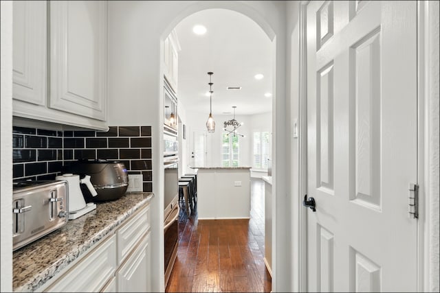 kitchen with arched walkways, tasteful backsplash, white cabinetry, and dark wood-style flooring