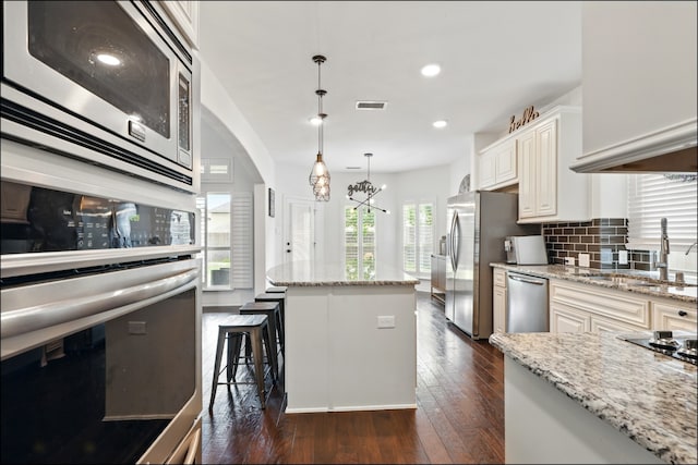 kitchen featuring stainless steel appliances, visible vents, a sink, light stone countertops, and a center island