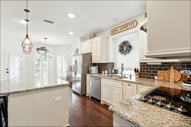 kitchen featuring stainless steel appliances, a center island, a sink, tasteful backsplash, and visible vents