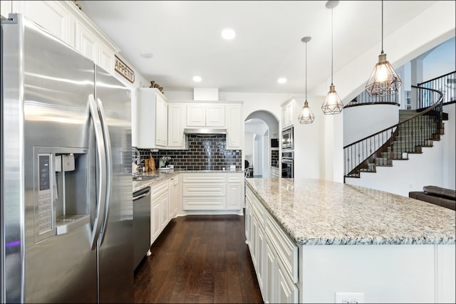 kitchen with light stone counters, arched walkways, appliances with stainless steel finishes, dark wood-style floors, and a kitchen island