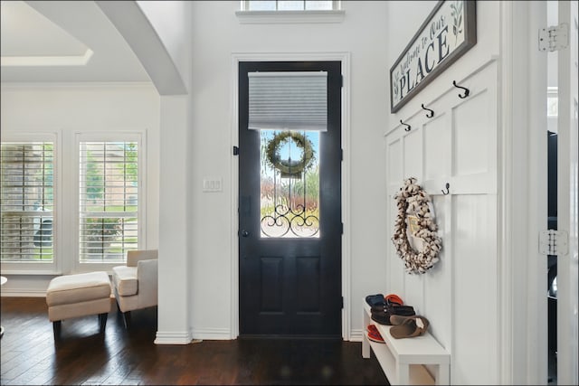 entryway with arched walkways, crown molding, dark wood-type flooring, and baseboards