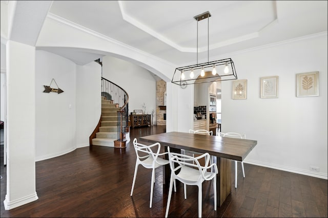 dining room featuring arched walkways, a tray ceiling, dark wood-style floors, and stairs