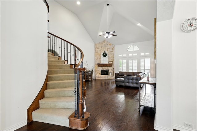 stairs featuring hardwood / wood-style floors, a ceiling fan, a stone fireplace, and high vaulted ceiling