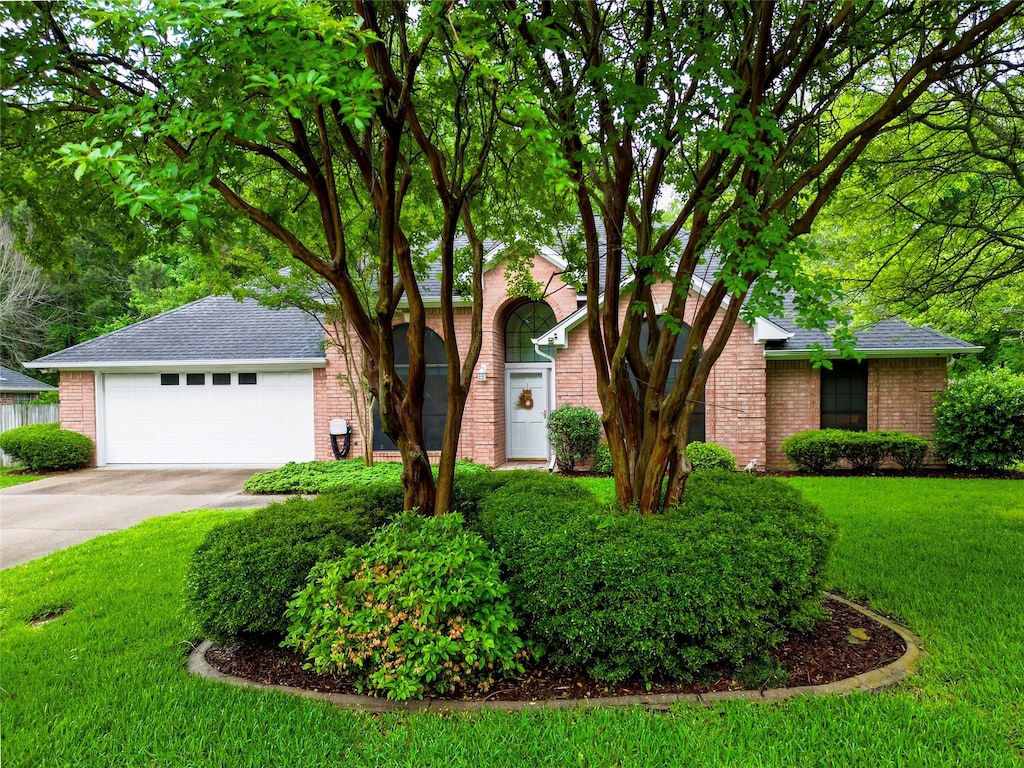 view of front of home with brick siding, a front yard, concrete driveway, and roof with shingles