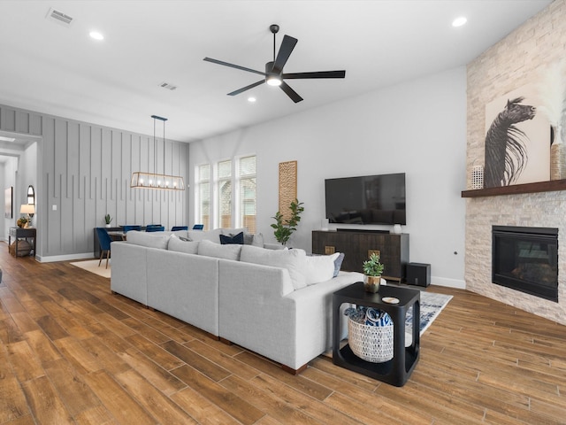 living area featuring a fireplace, wood finished floors, visible vents, and ceiling fan with notable chandelier