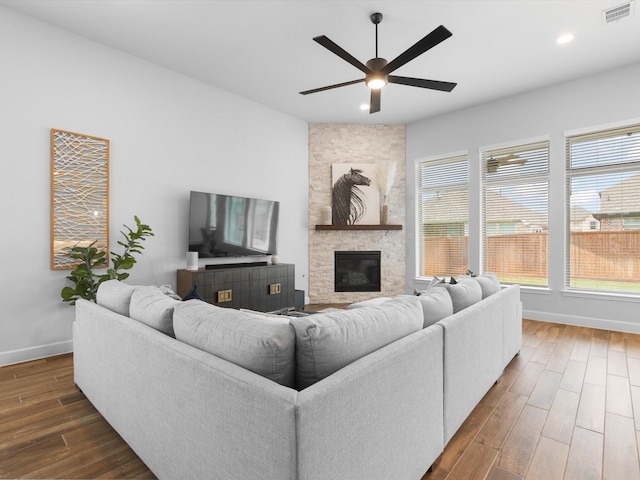 living area featuring visible vents, ceiling fan, baseboards, dark wood finished floors, and a stone fireplace