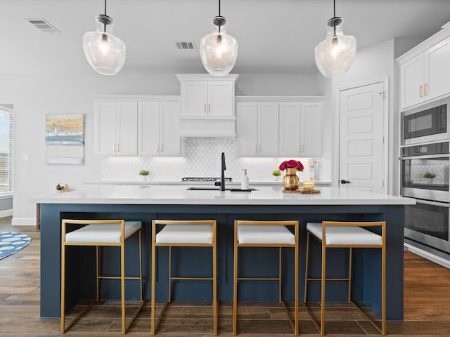 kitchen with built in microwave, stainless steel double oven, a sink, backsplash, and white cabinetry