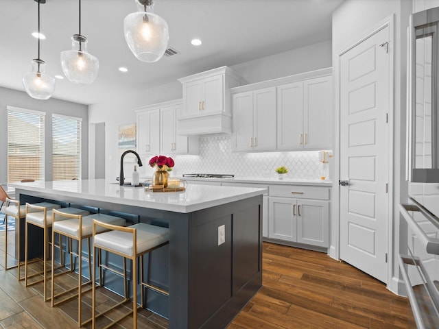 kitchen featuring a sink, a kitchen island with sink, white cabinets, and backsplash