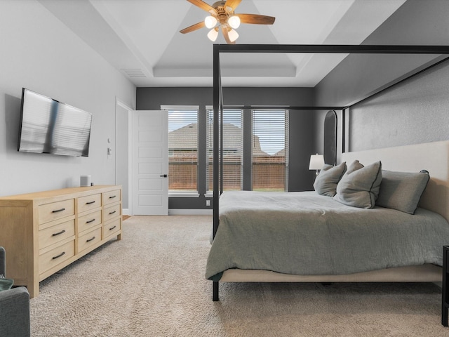 bedroom with a ceiling fan, visible vents, light colored carpet, and a tray ceiling