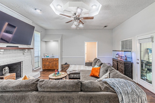 living room featuring ceiling fan, a brick fireplace, a textured ceiling, dark wood finished floors, and visible vents