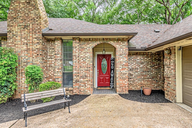 view of exterior entry with brick siding, a chimney, and roof with shingles
