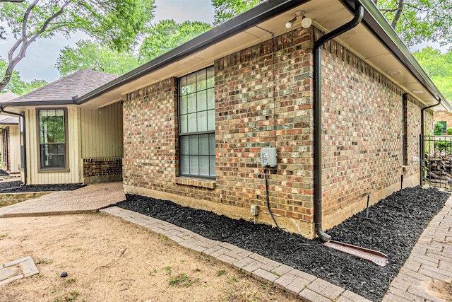 view of side of home with brick siding, fence, and a shingled roof