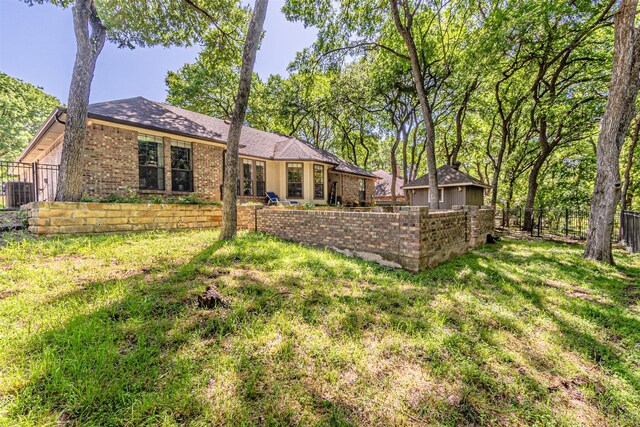 rear view of house with a fenced backyard, central air condition unit, a yard, and brick siding