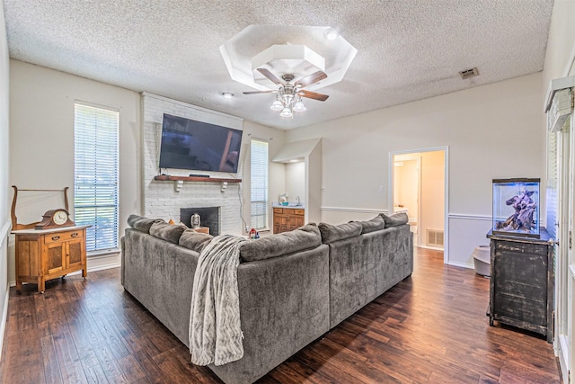 living room featuring ceiling fan, dark wood-style flooring, a textured ceiling, visible vents, and a fireplace