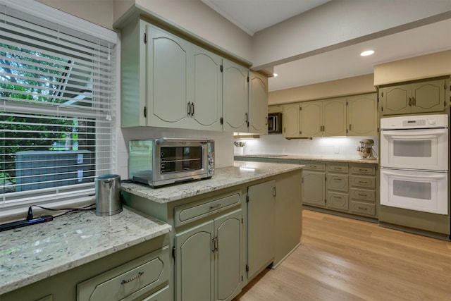 kitchen featuring a toaster, double oven, stainless steel microwave, light wood-style flooring, and backsplash