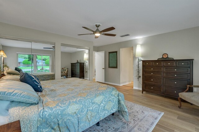 bedroom featuring light wood finished floors, multiple closets, a ceiling fan, baseboards, and visible vents