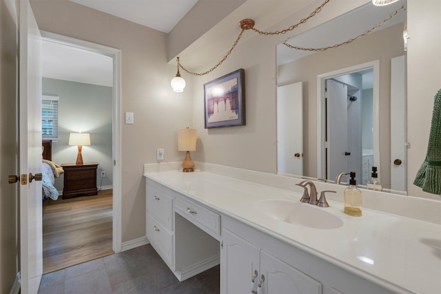 ensuite bathroom with connected bathroom, tile patterned floors, baseboards, and vanity