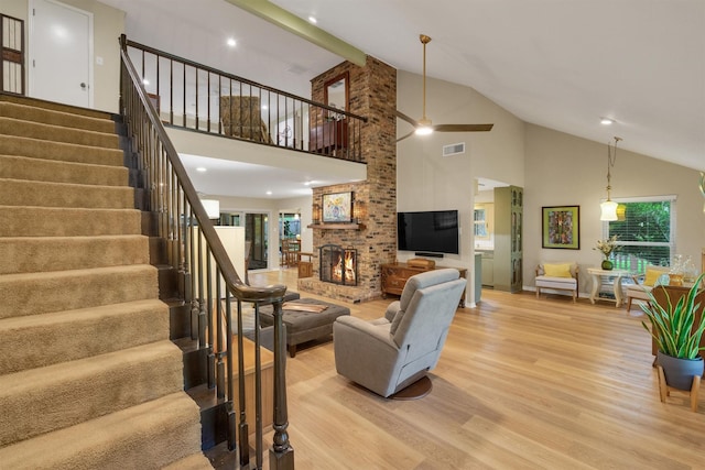 living room with ceiling fan, a fireplace, high vaulted ceiling, light wood-style floors, and stairs