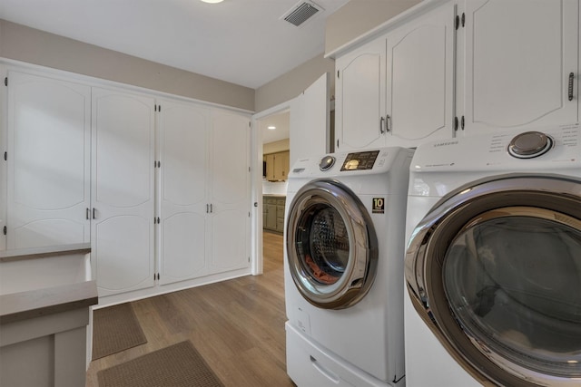 laundry area featuring light wood-style floors, visible vents, cabinet space, and washing machine and clothes dryer