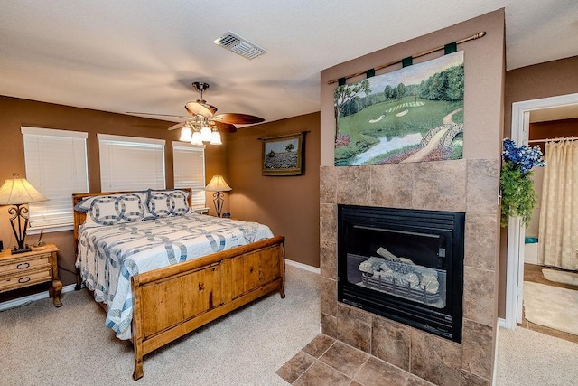 bedroom featuring a tile fireplace, ceiling fan, carpet flooring, baseboards, and visible vents