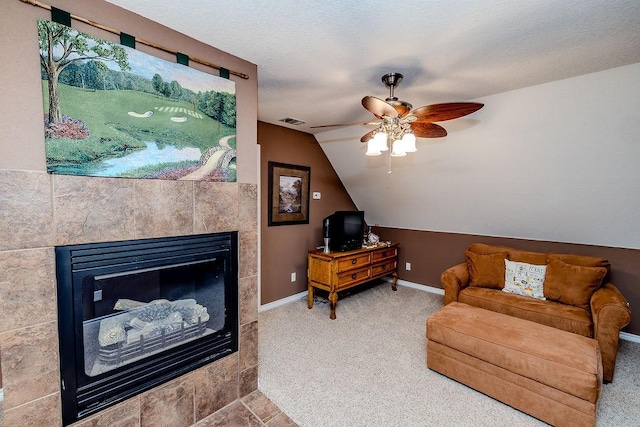 carpeted living area with a tile fireplace, ceiling fan, baseboards, visible vents, and lofted ceiling