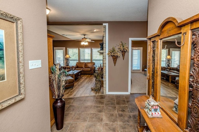 entryway with dark tile patterned floors, a textured wall, baseboards, a ceiling fan, and a textured ceiling