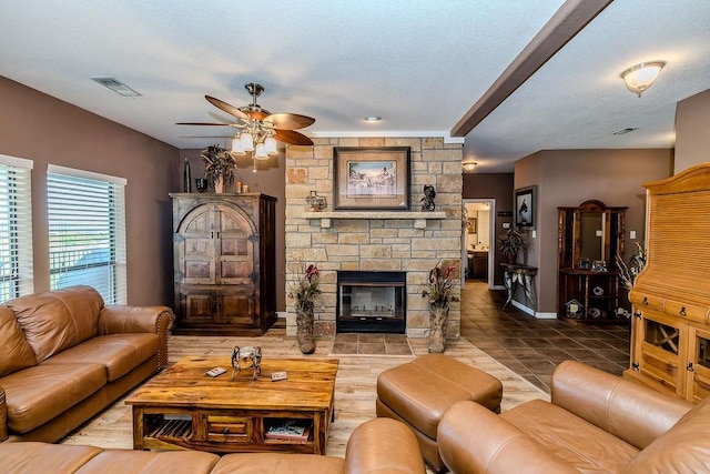 tiled living room featuring a textured ceiling, visible vents, baseboards, a ceiling fan, and a stone fireplace