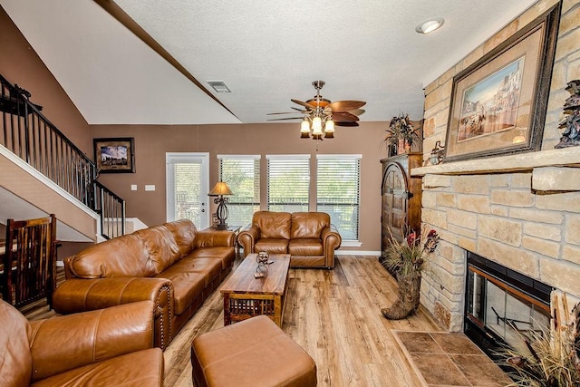 living room featuring visible vents, wood finished floors, a ceiling fan, a stone fireplace, and stairs