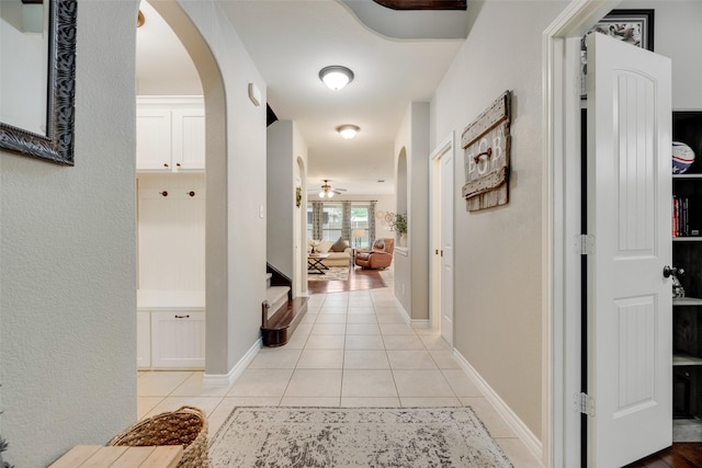 hall featuring light tile patterned flooring, arched walkways, stairs, and baseboards