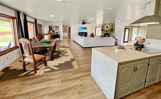 712 State Highway 67, Graham, TX 76450 - kitchen featuring light wood-style flooring, black electric stovetop, a large fireplace, wall chimney exhaust hood, and a ceiling fan