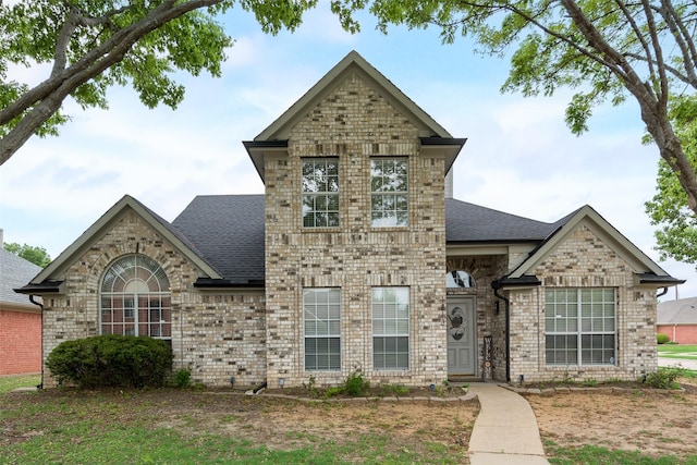 french country inspired facade featuring brick siding and a shingled roof