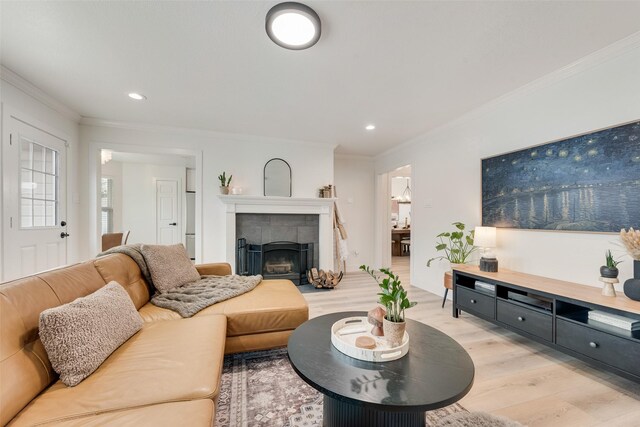 living room featuring a tiled fireplace, recessed lighting, light wood-style floors, and crown molding