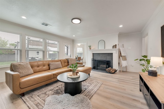 living area with a tile fireplace, ornamental molding, light wood-type flooring, baseboards, and visible vents