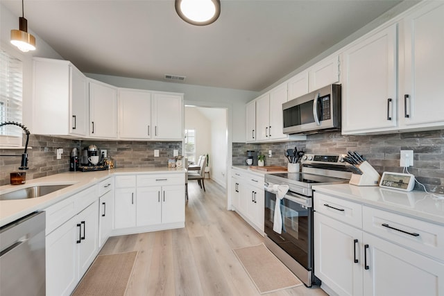kitchen featuring white cabinetry, a sink, appliances with stainless steel finishes, light wood-style floors, and backsplash