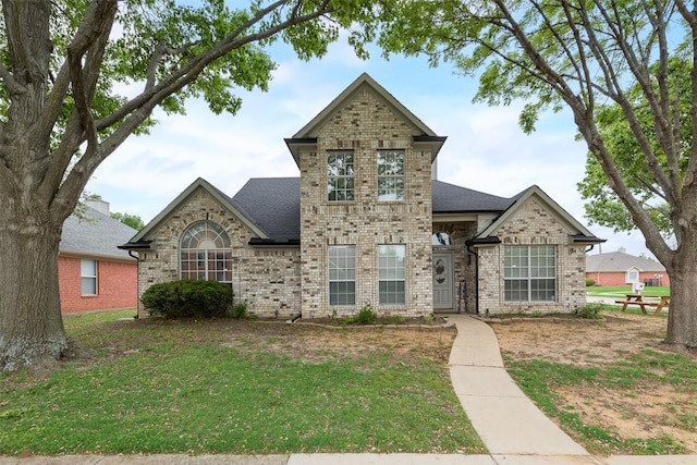 french country inspired facade with roof with shingles, a front lawn, and brick siding